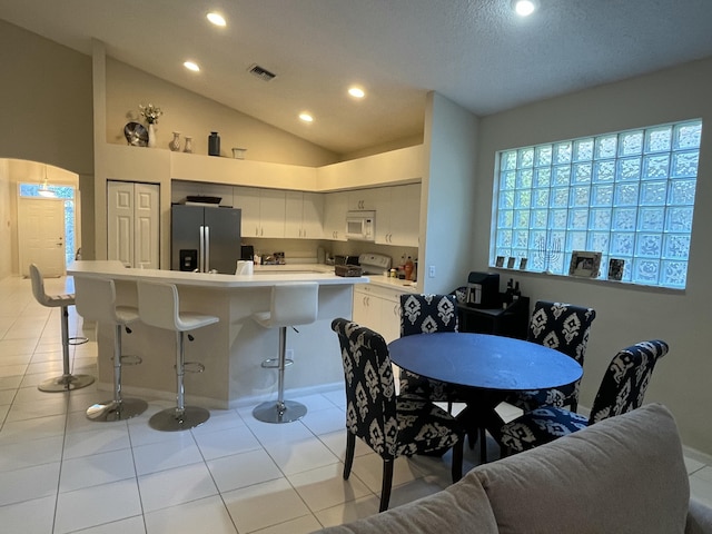 kitchen with lofted ceiling, stove, a kitchen breakfast bar, stainless steel refrigerator with ice dispenser, and white cabinets