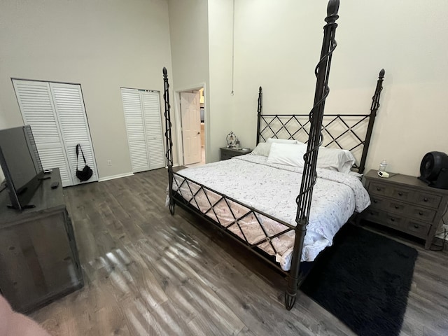 bedroom with two closets, dark hardwood / wood-style floors, and a high ceiling