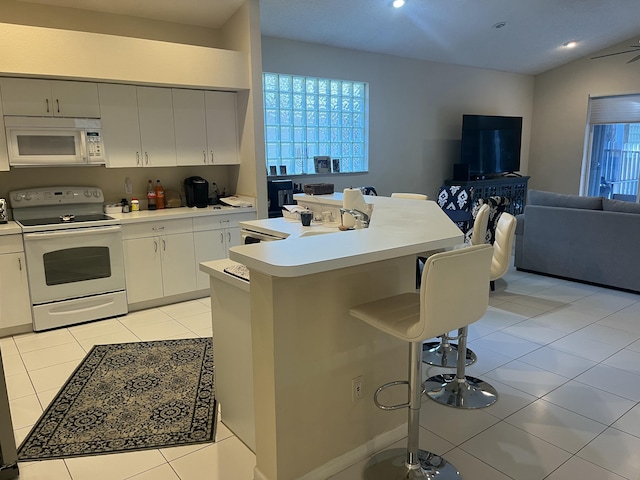 kitchen featuring a breakfast bar area, white cabinets, a kitchen island with sink, light tile patterned floors, and white appliances