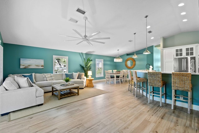 living room with lofted ceiling, ceiling fan, and light wood-type flooring