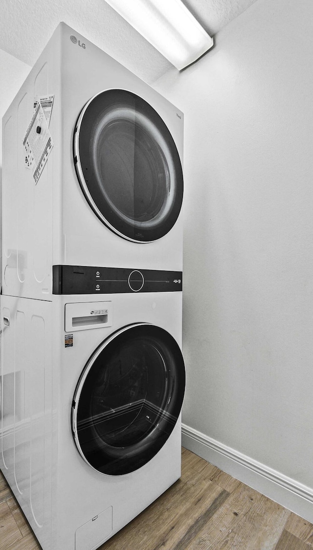 clothes washing area featuring hardwood / wood-style floors, stacked washer / drying machine, and a textured ceiling