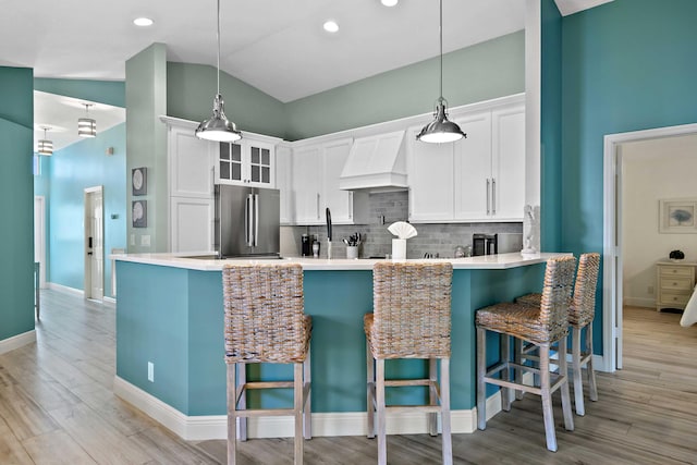 kitchen featuring white cabinetry, stainless steel refrigerator, lofted ceiling, and custom range hood