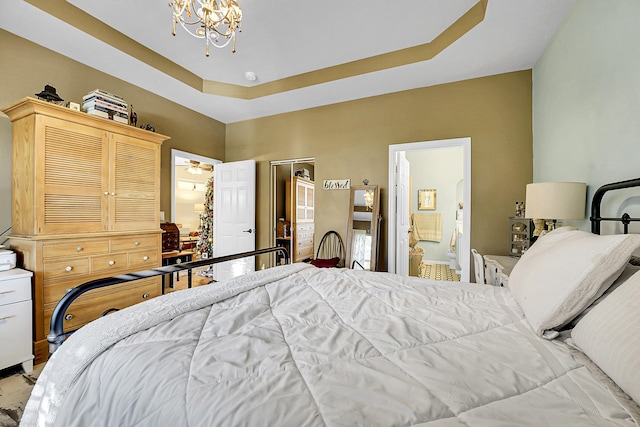 bedroom featuring a raised ceiling, connected bathroom, and an inviting chandelier