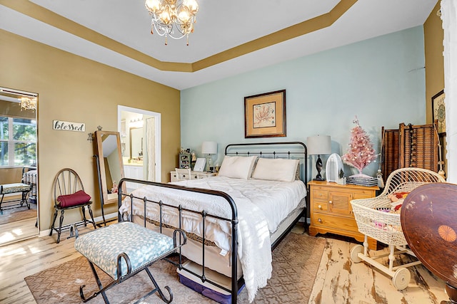 bedroom featuring a raised ceiling, ensuite bath, light hardwood / wood-style flooring, and a chandelier