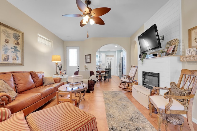 living area featuring a ceiling fan, arched walkways, light tile patterned flooring, and a fireplace