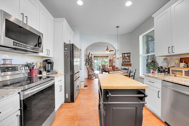 kitchen with light tile patterned floors, arched walkways, appliances with stainless steel finishes, wooden counters, and backsplash