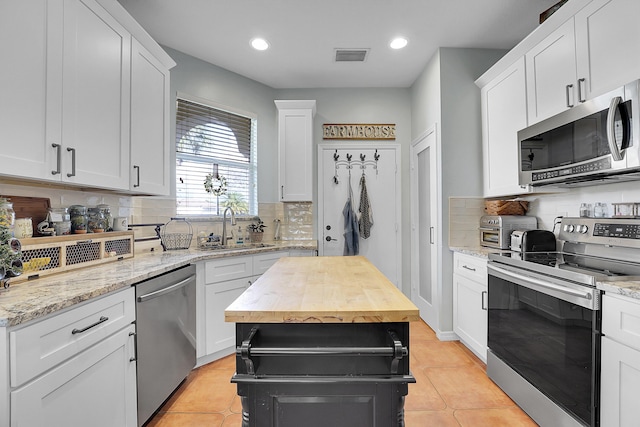 kitchen with light tile patterned floors, stainless steel appliances, visible vents, white cabinets, and a sink