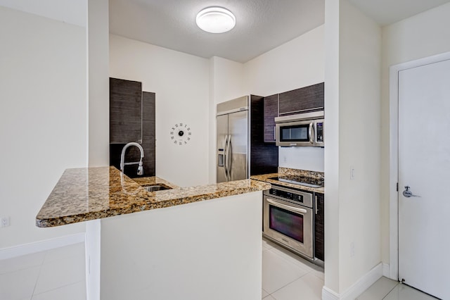 kitchen with kitchen peninsula, appliances with stainless steel finishes, sink, light tile patterned floors, and stone countertops