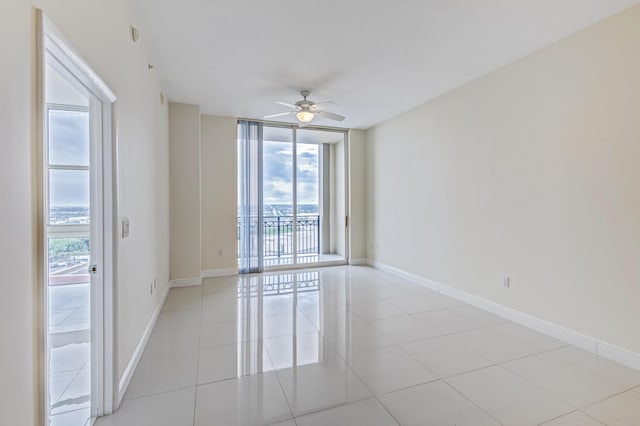 spare room featuring ceiling fan, light tile patterned flooring, and a wall of windows