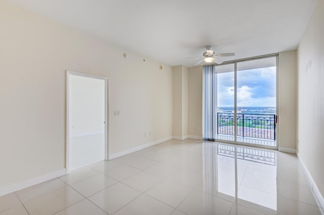 tiled empty room with ceiling fan and a wall of windows