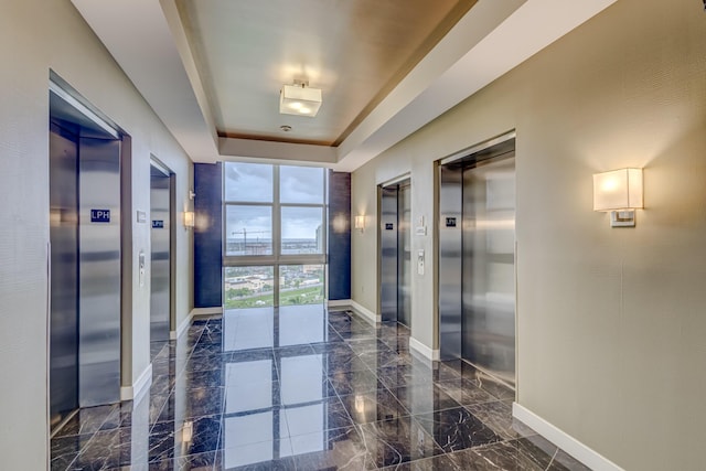 hallway featuring a tray ceiling, elevator, and floor to ceiling windows