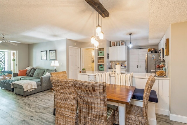 dining room with ceiling fan, beam ceiling, light wood-type flooring, and a textured ceiling