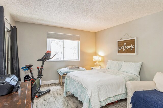 bedroom with access to exterior, light hardwood / wood-style flooring, multiple windows, and a textured ceiling