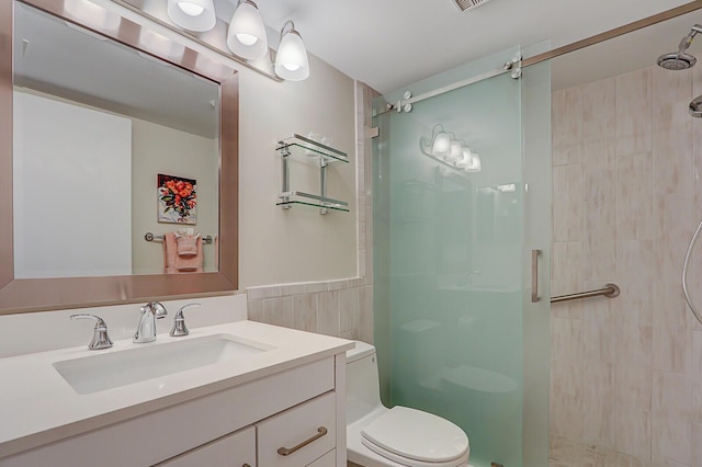 bathroom with a tile shower, vanity, toilet, and tile walls