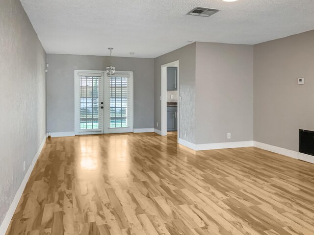 unfurnished living room with french doors, a textured ceiling, and a notable chandelier