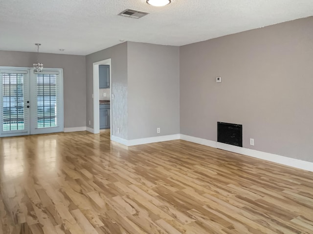 unfurnished living room with french doors, a textured ceiling, light hardwood / wood-style floors, and a notable chandelier