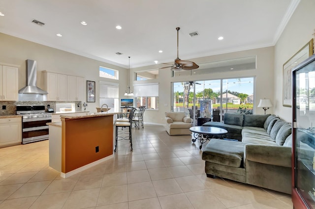 kitchen featuring white cabinetry, stainless steel range, wall chimney exhaust hood, ceiling fan, and a kitchen bar