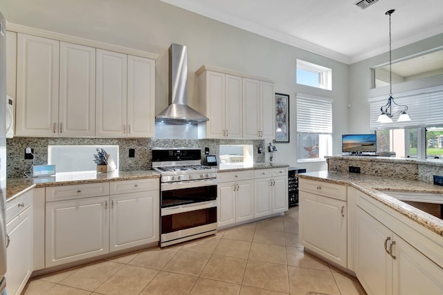 kitchen with backsplash, wall chimney exhaust hood, light tile patterned floors, a chandelier, and stainless steel range with gas stovetop