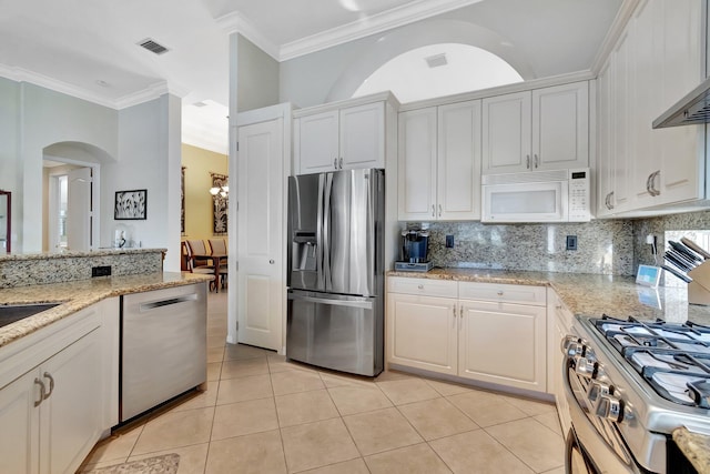 kitchen with light stone countertops, appliances with stainless steel finishes, backsplash, light tile patterned floors, and white cabinets