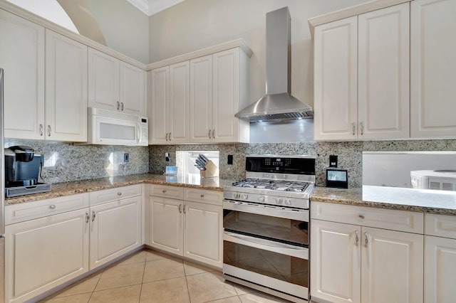 kitchen with gas range, light tile patterned floors, wall chimney range hood, backsplash, and white cabinets