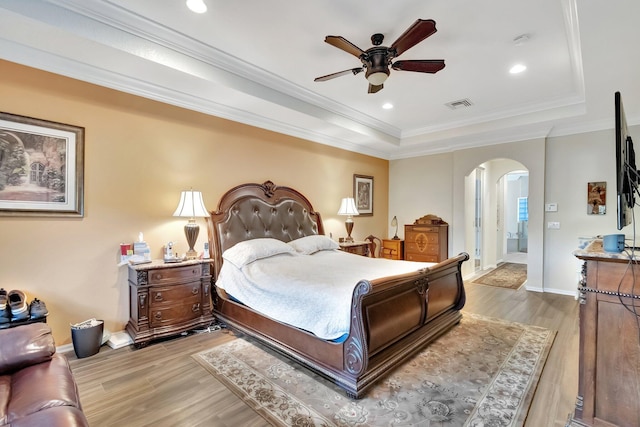 bedroom with ornamental molding, a tray ceiling, ceiling fan, and light hardwood / wood-style floors