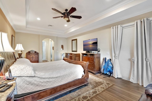 bedroom with ceiling fan, light hardwood / wood-style floors, a raised ceiling, and ornamental molding