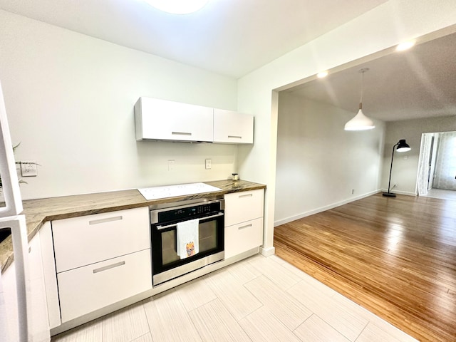 kitchen with electric stovetop, pendant lighting, oven, white cabinetry, and butcher block counters