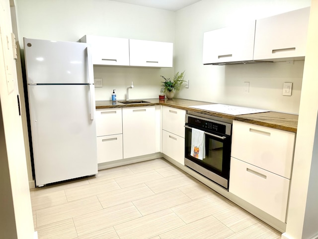 kitchen featuring white fridge, cooktop, stainless steel oven, and white cabinetry