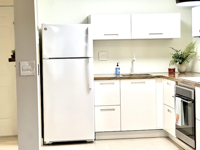 kitchen featuring white cabinets, oven, sink, light tile patterned floors, and white fridge