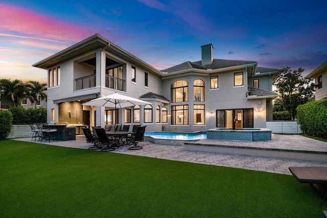 back house at dusk featuring a pool with hot tub, a yard, and a patio