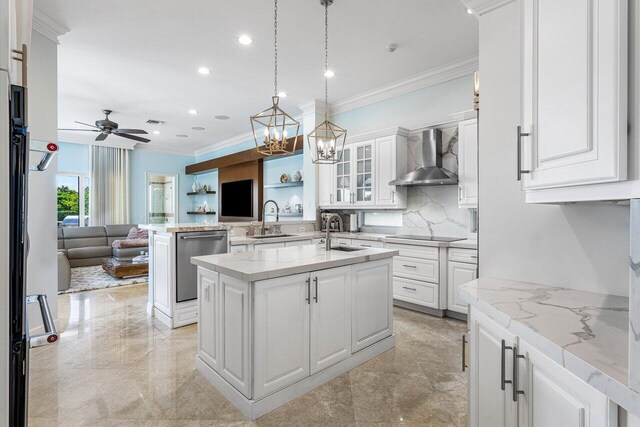 kitchen featuring dishwasher, wall chimney exhaust hood, an island with sink, white cabinets, and ceiling fan with notable chandelier