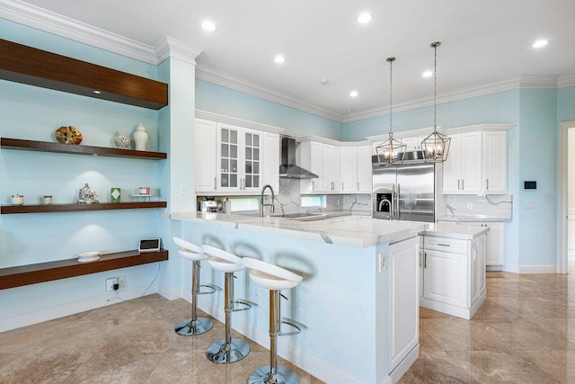 kitchen with stainless steel built in refrigerator, decorative light fixtures, white cabinets, and wall chimney exhaust hood