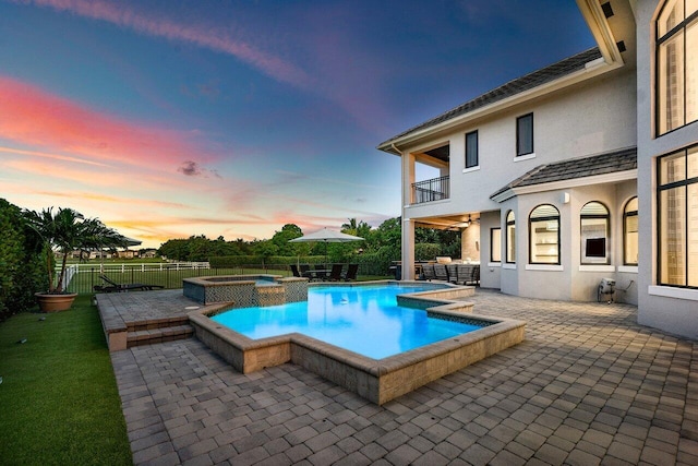 pool at dusk with a jacuzzi, ceiling fan, and a patio