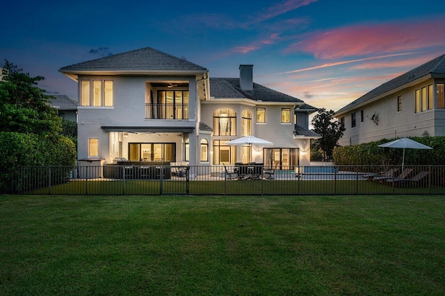 back house at dusk featuring a balcony, a patio area, a yard, and a swimming pool