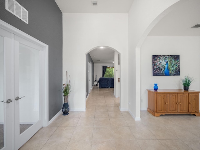 hallway with light tile patterned floors, baseboards, visible vents, and arched walkways