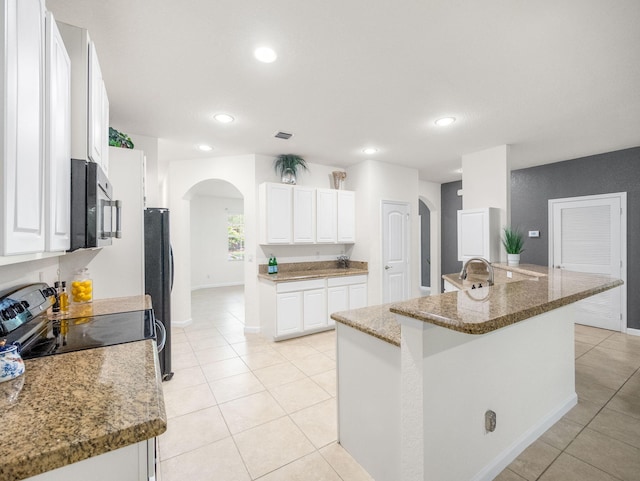 kitchen with stainless steel appliances, arched walkways, white cabinetry, and light tile patterned flooring