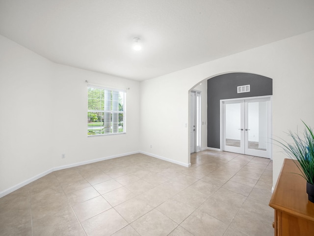 unfurnished room with light tile patterned floors, baseboards, visible vents, arched walkways, and french doors