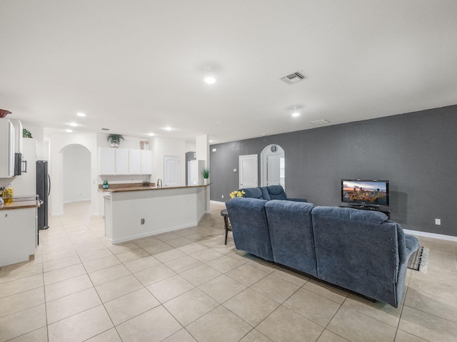 living room featuring arched walkways, light tile patterned flooring, visible vents, and baseboards