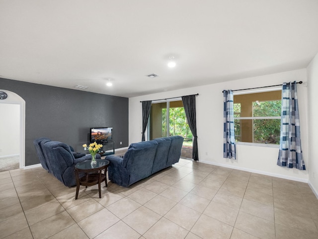 living area with light tile patterned floors, arched walkways, visible vents, and baseboards