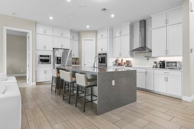 kitchen featuring white cabinetry, a center island with sink, wall chimney exhaust hood, and stainless steel appliances