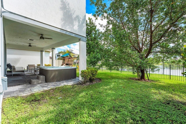 view of yard with a water view, ceiling fan, a playground, a patio, and a hot tub