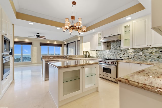 kitchen featuring light stone countertops, stainless steel appliances, a tray ceiling, white cabinets, and hanging light fixtures