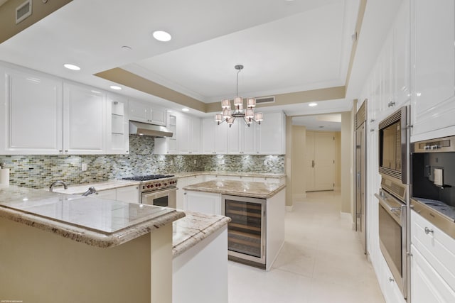 kitchen featuring pendant lighting, white cabinets, appliances with stainless steel finishes, a tray ceiling, and beverage cooler