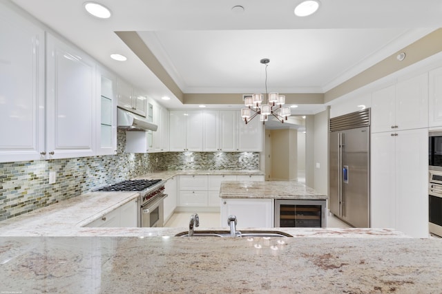 kitchen with built in appliances, light stone counters, white cabinets, and pendant lighting