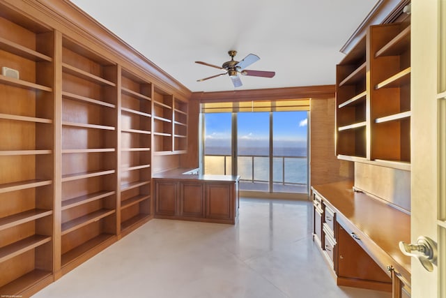 unfurnished office with built in shelves, built in desk, a water view, and ceiling fan