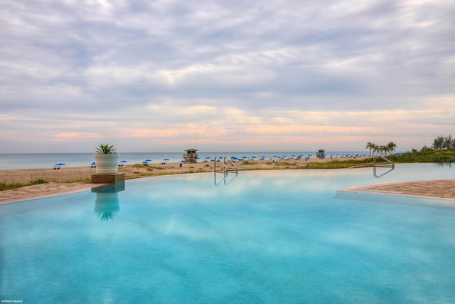 pool at dusk featuring a water view and a view of the beach