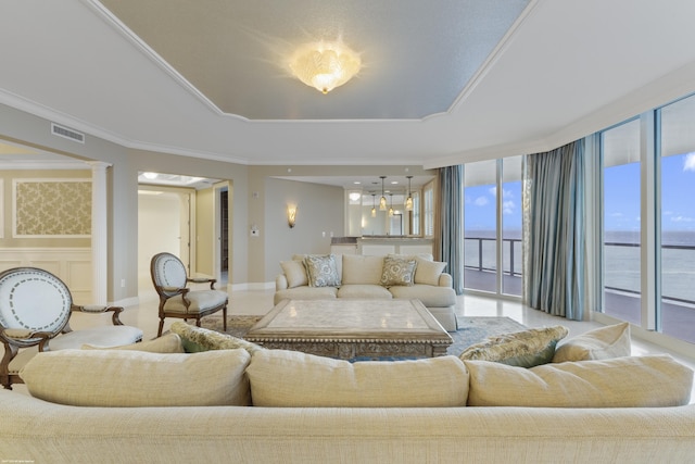 living room with expansive windows, a raised ceiling, a water view, crown molding, and ornate columns