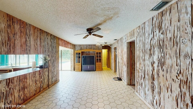 unfurnished living room with sink, ceiling fan, and wood walls