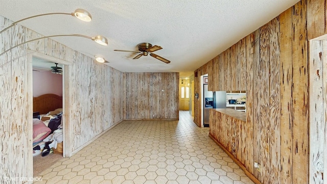 interior space with ceiling fan, a textured ceiling, and wood walls