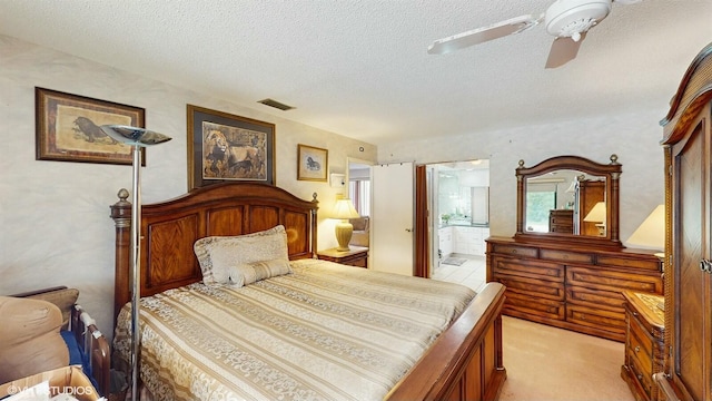 bedroom with ceiling fan, light colored carpet, a textured ceiling, and ensuite bath